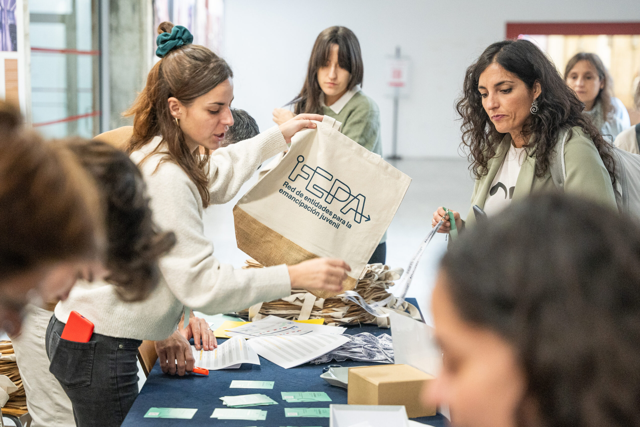Mesa de acreditaciones de la 18º edición de las jornadas FEPA. Una técnica de la entidad entrega una totebag corporativa a una de las personas asistentes.