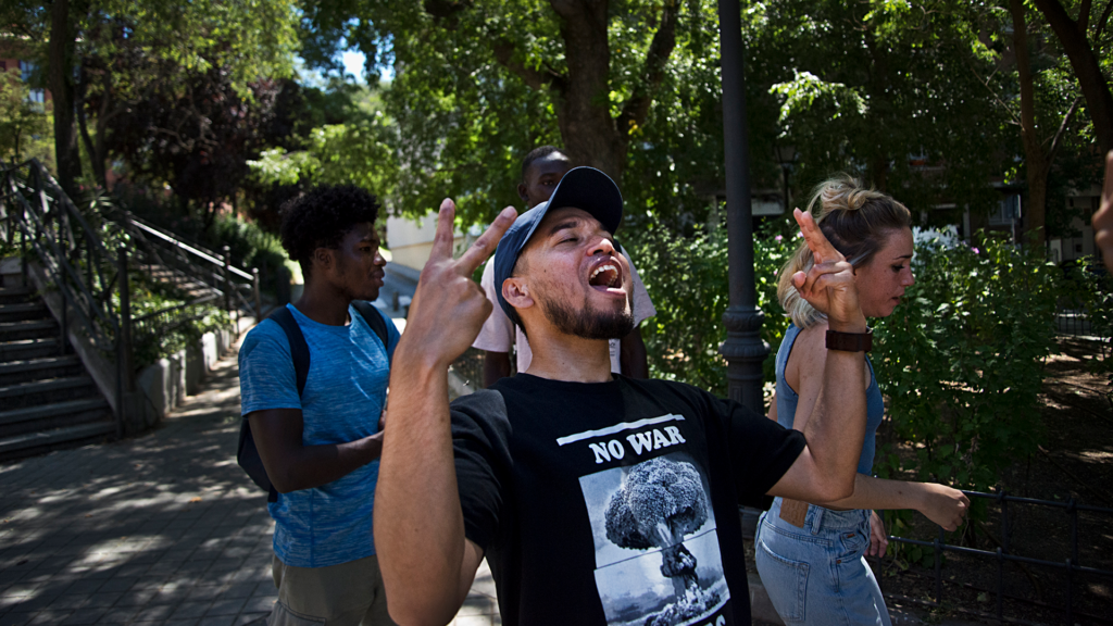 Un grupo de tres jóvenes extutelados camina en grupo por la calle, acompañados de su referente. Uno de ellos, hace el signo de la victoria con las dos manos y mira al cielo.